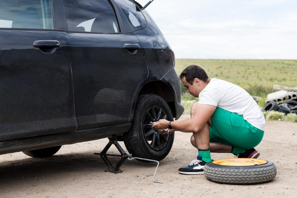 man fixing a car with a flat tire