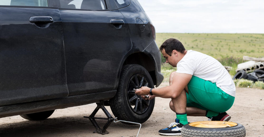 man fixing a car with a flat tire